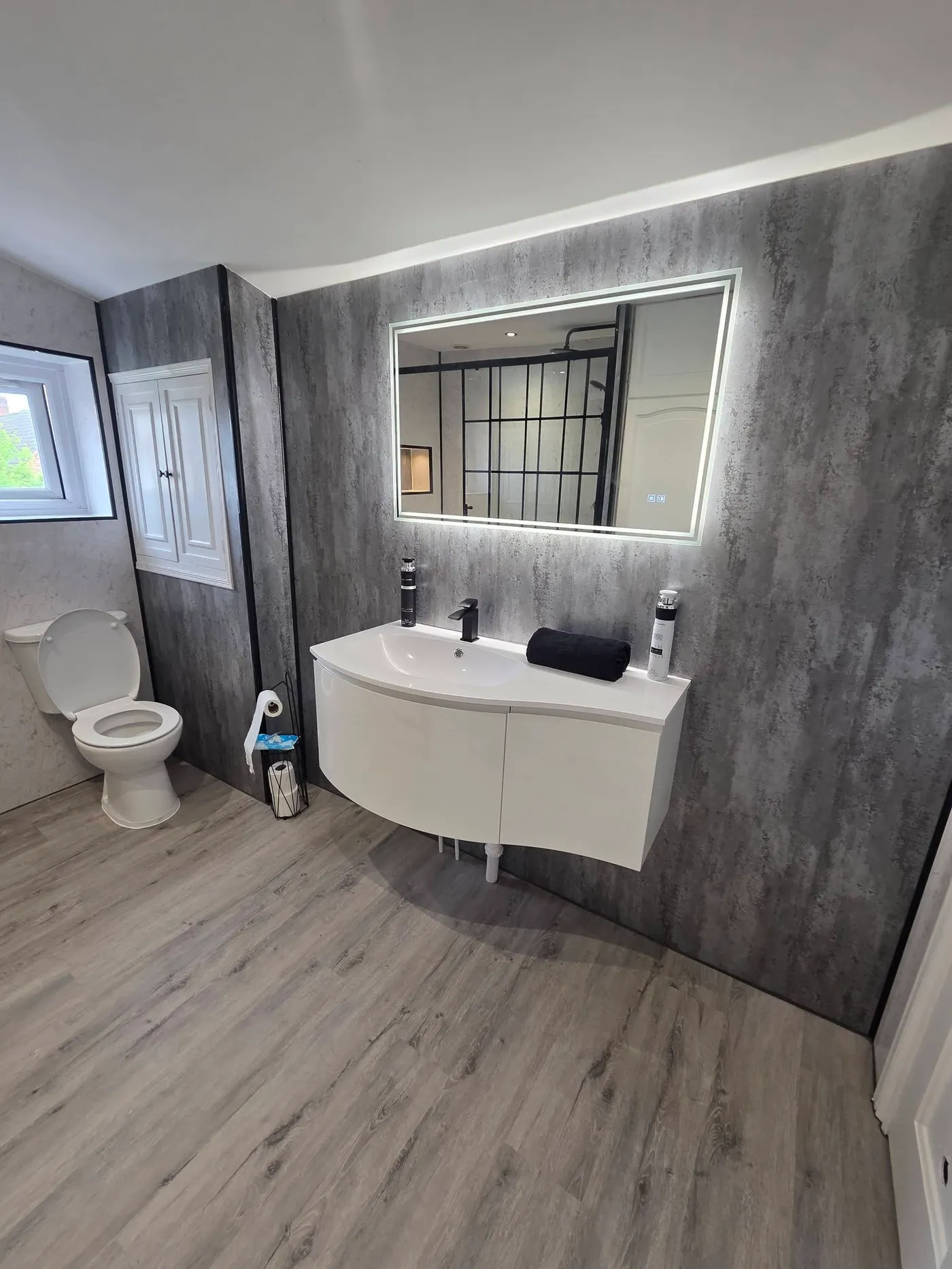 The finished bathroom with a centred basin, toilet and new wood-effect flooring.