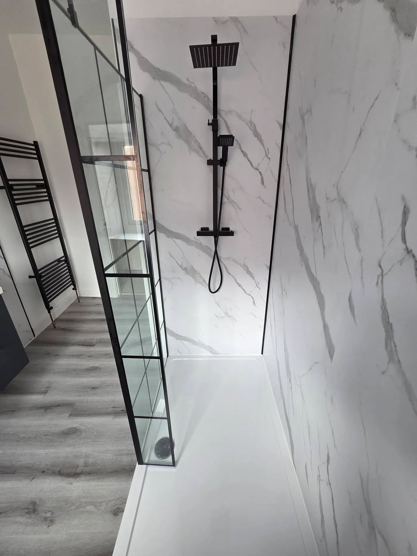 The completed shower with black fittings, a grid screen and marble-effect panels.