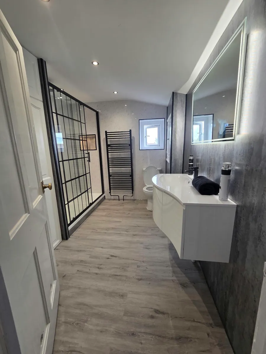 Bathroom with a black-framed shower screen, white wall-hung vanity, illuminated mirror and black towel radiator.