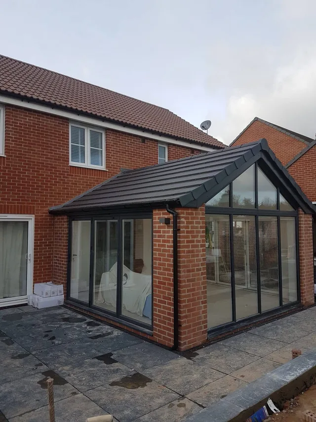 Red-brick extension with a dark tiled pitched roof, glazed gable and dark-framed glass doors.